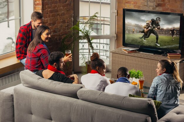 Excited group of people watching american football, sport match at home.