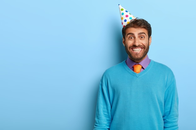 파란색 스웨터에 포즈 생일 모자와 흥분된 남자