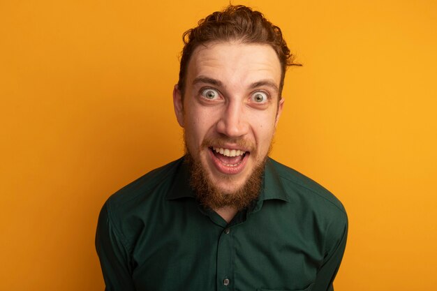 Excited handsome blonde man looks at front isolated on orange wall