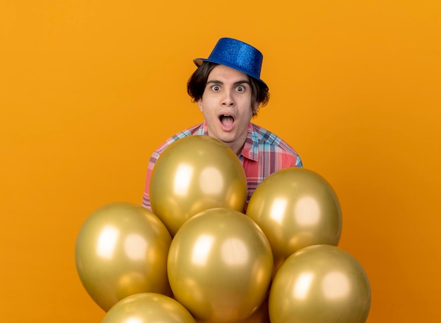 Free photo excited handsome caucasian man wearing blue party hat stands with helium balloons