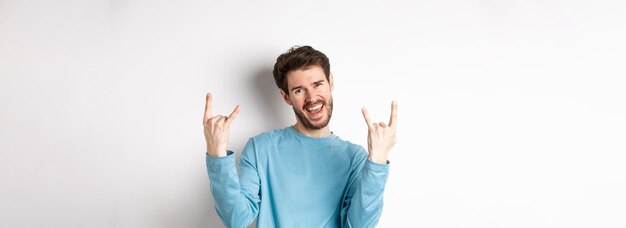 Excited handsome man celebrating having fun and showing rock on horns gesture enjoing party smiling