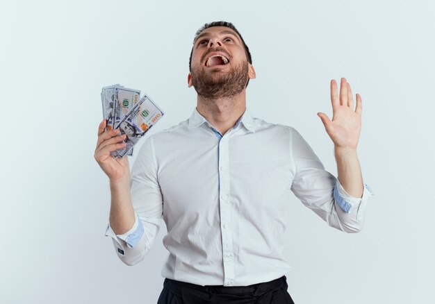 Excited handsome man holds money and raises hand looking up isolated on white wall