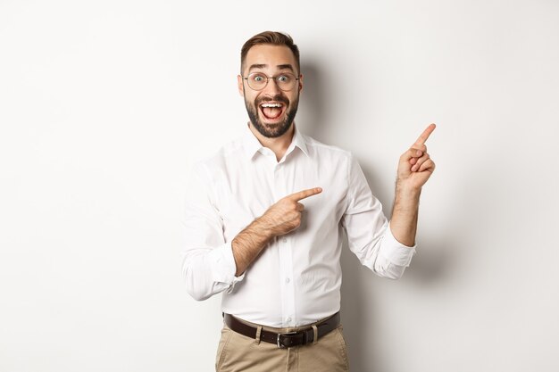 Excited handsome man pointing fingers at upper right corner, showing logo, standing  white