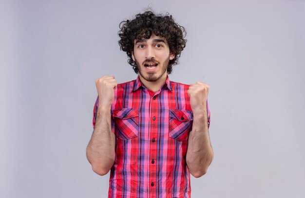 An excited handsome man with curly hair in checked shirt raising clenched fists 