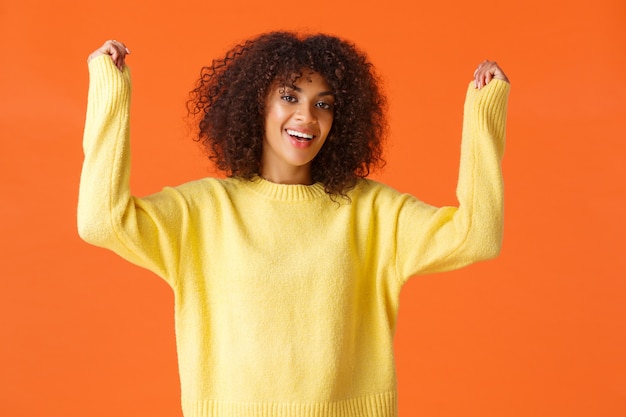 アフロヘアカットで興奮した幸せなアフリカ系アメリカ人の少女は、興奮と幸福から手を上げ、勝利を応援し、勝利を祝います。