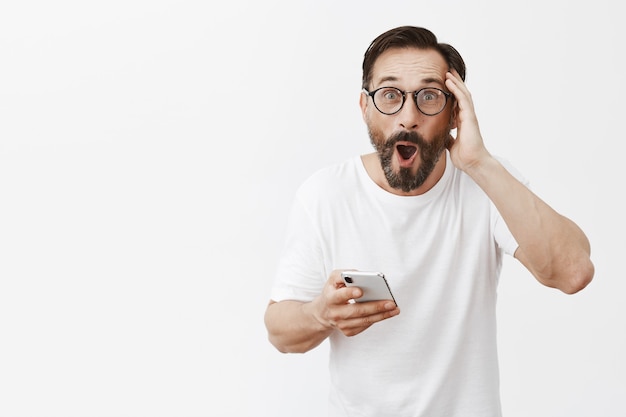 Excited and happy bearded mature man posing with his phone
