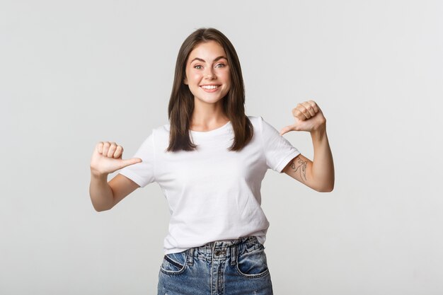 Excited happy brunette girl smiling, pointing fingers at your logo, showing banner.