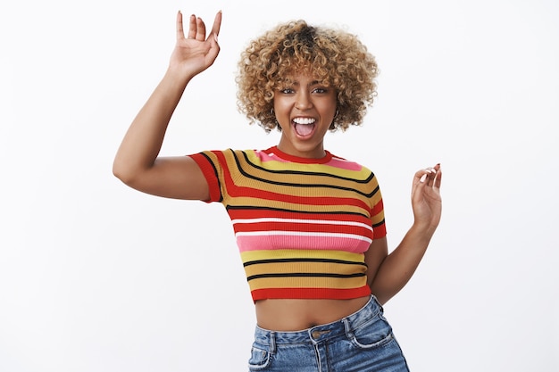 Free photo excited and happy girl having fun at party yelling from joy and thrill as dancing, enjoying cool music raising hands smiling broadly feeling awesome over white wall in stylish 90s outfit