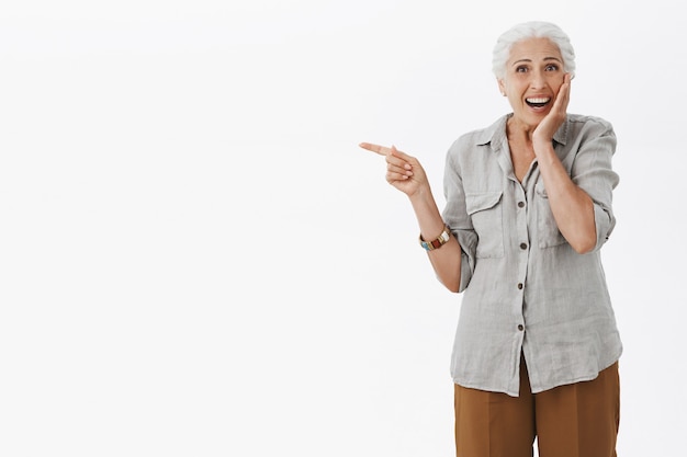 Eccitato nonna felice che punta il dito a sinistra e sorridente stupito