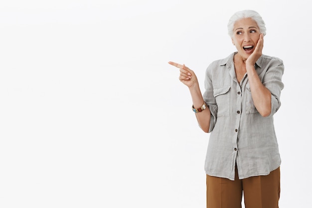 Free photo excited happy granny pointing finger left and smiling amazed