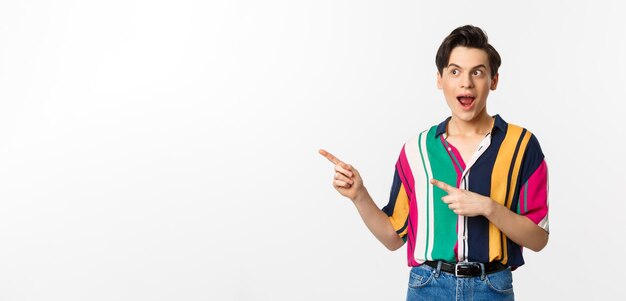 Excited happy man pointing left at promo banner looking amazed standing against white background