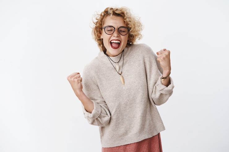 無料Photo 幸せと喜びから大声で叫ぶ興奮した幸せでスリル満点の美しい若い女性は、喜びとお祝いで拳を握り締め、目標を達成することに勝利し、夢から喜びを実現しました。