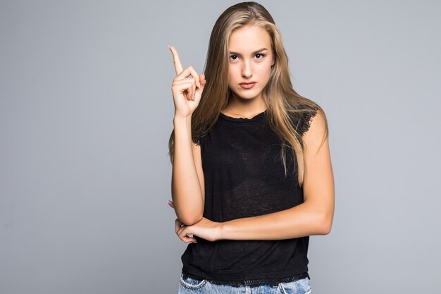 Excited happy woman holding tablet computer and pointing finger up at copy space while standing isolated over gray background