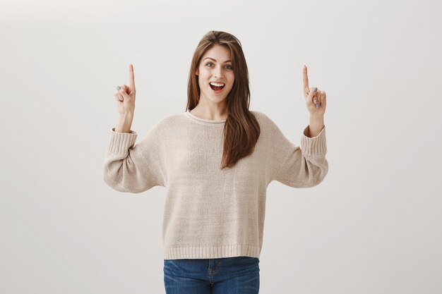 Excited happy woman showing promo with pleased smile, pointing fingers up