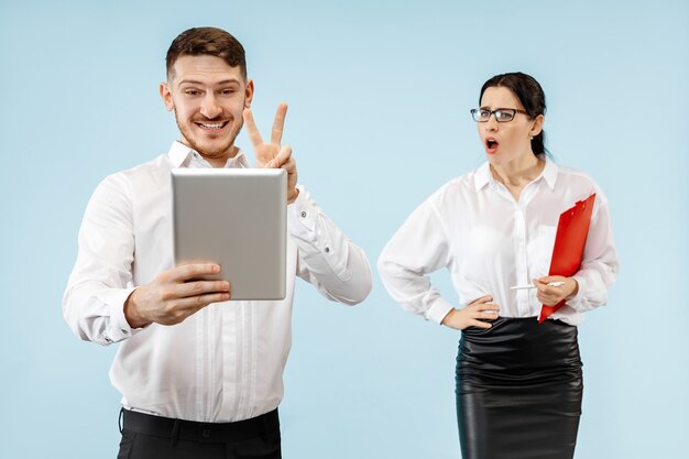 Excited happy young couple looking at camera with delight. Businessman and woman isolated on blue studio background