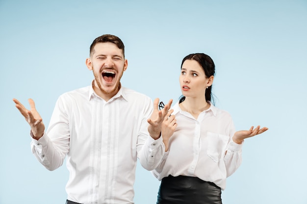 Excited happy young couple looking at camera with delight. Businessman and woman isolated on blue studio background