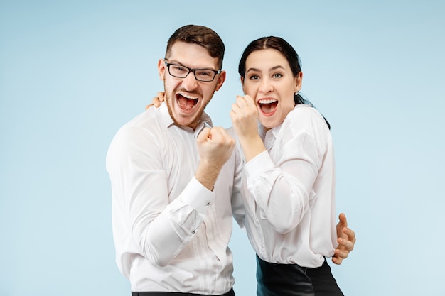 Excited happy young couple looking at camera with delight. Businessman and woman isolated on blue studio background