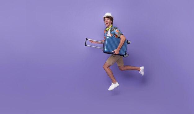 Excited happy young man tourist with luggage jumping isolated on purple studio background