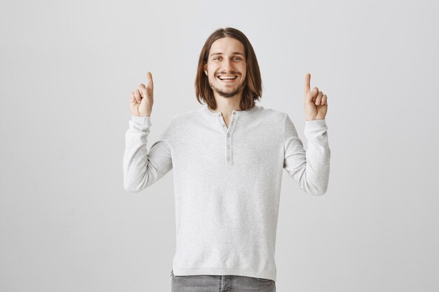 Excited hipster guy pointing fingers up and smiling