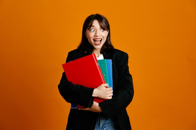 excited holding folders young beautiful female wearing black jacket isolated on orange background