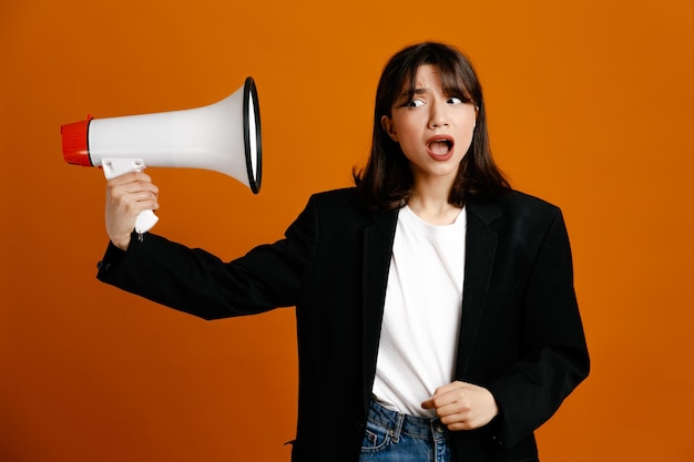 Free photo excited holding loudspeaker young beautiful female wearing black jacket isolated on orange background