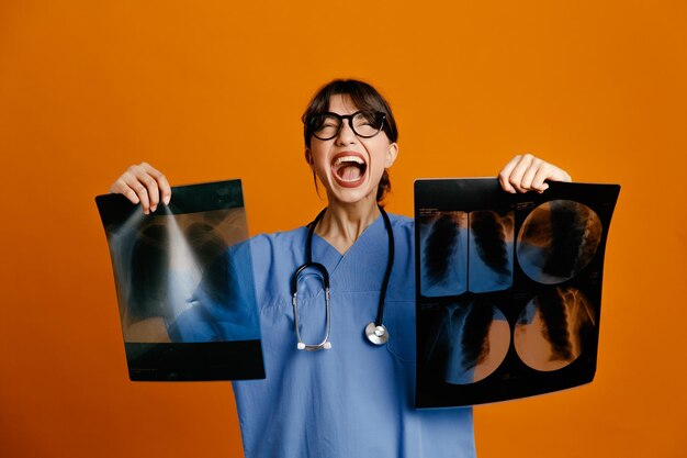 Eccitato holding xray giovane dottoressa che indossa uno stetoscopio fith uniforme isolato su sfondo arancione