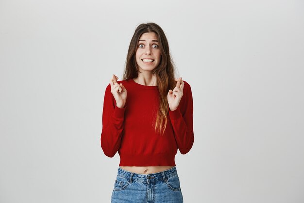 Excited and hopeful pretty female student cross fingers as making wish, pleading