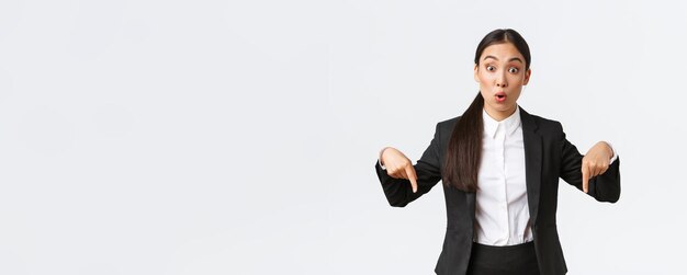 Excited and impressed asian female broker pointing fingers down showing big deal astounded businessw