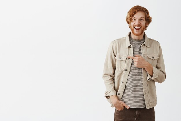 Excited and impressed bearded redhead guy posing against the white wall