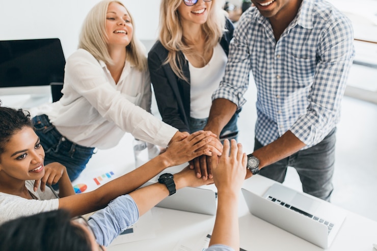 Free Photo excited international students in casual attires ready for team work. indoor portrait of glad mulatto girl with curly hair holding hands with european lady and african young man in office.