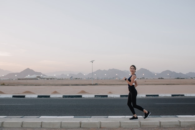 Excited joyful amazing happy woman running on road of tropical country. Smiling, expressing positivity, true emotions, healthy lifestyle, workout..