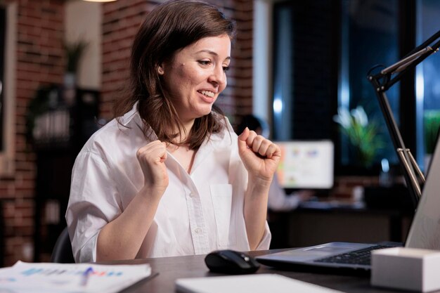 Excited joyful financial advisor celebrating succesful business deal while sitting at desk in office workspace. Happy excited businesswoman smiling with joy because of positive promoting campaign.