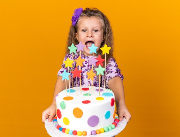 들고와 복사 공간 오렌지 벽에 고립 된 생일 케이크를보고 흥분된 작은 금발 소녀