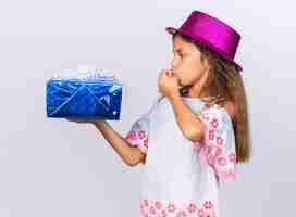 Free photo excited little caucasian girl with purple party hat holding gift box and kissing fingers isolated on white wall with copy space