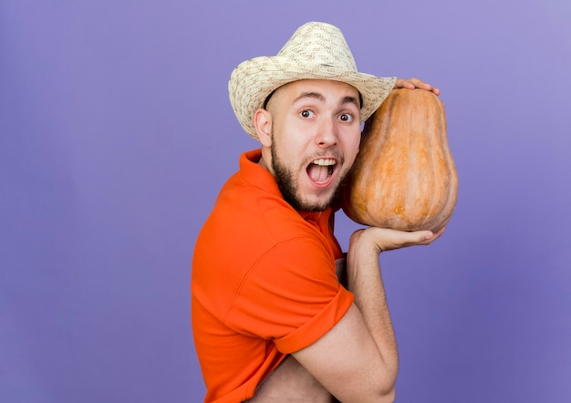 Il giardiniere maschio emozionante che porta il cappello di giardinaggio tiene lo sguardo della zucca