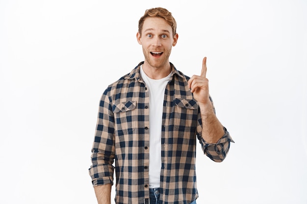 Excited man pitching great idea, smiling pleased and raising finger up to say something genius, got plan, have suggestion, standing over white wall