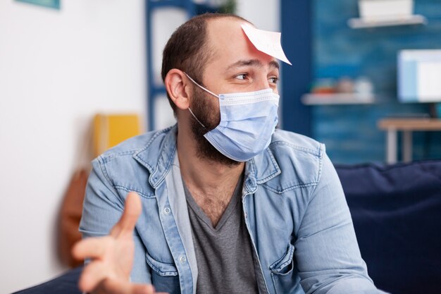 Excited man playing name game with multiethnic friends wearing face mask to keeping social distancing due to social pandemic having fun. Conceptual image.