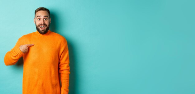 Excited man pointing at himself looking amazed and happy being chosen standing over light blue backg