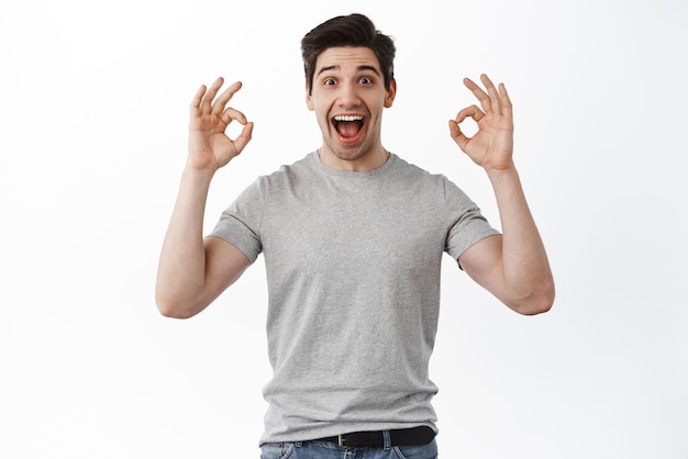 Free photo excited man screams with joy and shows okay signs rate super cool thing praise excellent thing rejoicing approve and like standing over white background