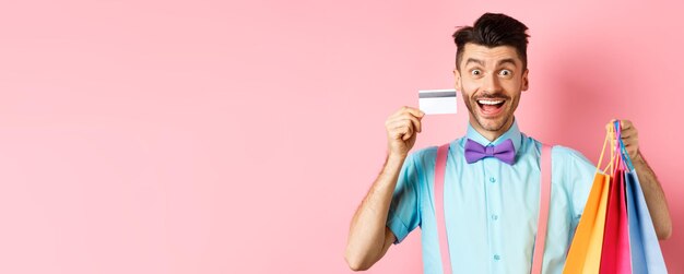 Free photo excited man showing plastic credit card and shopping bags smiling amazed while buying gifts standing