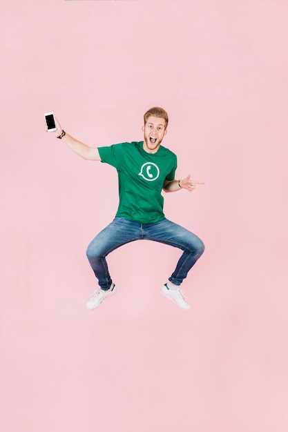 Free photo excited man with smartphone jumping on pink backdrop