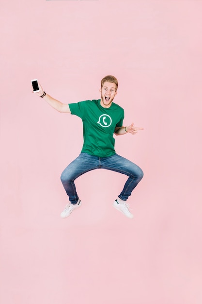 Excited man with smartphone jumping on pink backdrop
