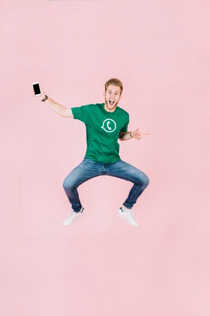 Возбужденный человек с смартфоном, прыгающий на розовом фоне