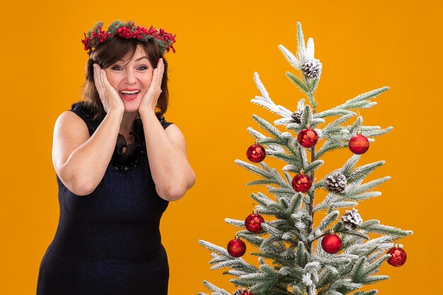 飾られたクリスマスツリーの近くに立っている首の周りにクリスマスの頭の花輪と見掛け倒しの花輪を身に着けている興奮した中年の女性