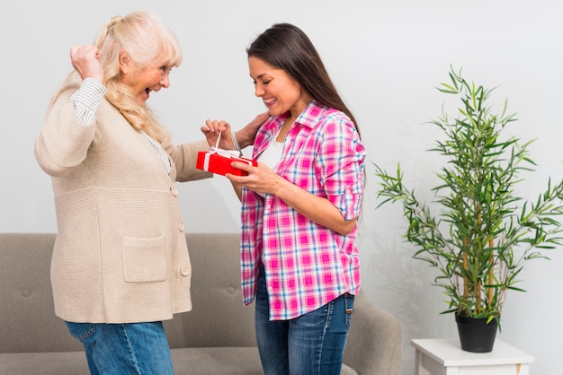 Excited mother looking at her daughter opening the red gift box at home