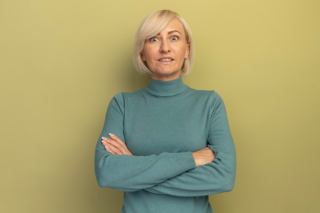 Excited pretty blonde slavic woman stands with crossed arms on olive green