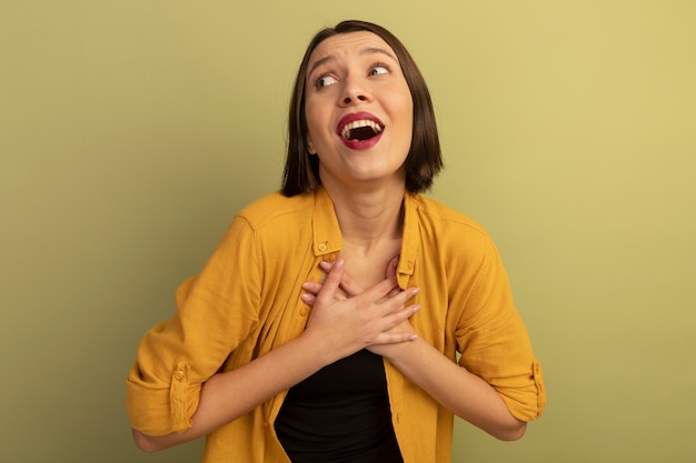 Eccitata donna abbastanza caucasica mette le mani sul petto e guarda a lato su verde oliva