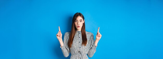 ドレスを着た興奮したきれいな女性が、広告に興味をそそられて「うわー」と言って、指をロゴに向けている