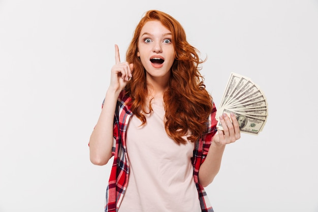 興奮してかなり若い赤毛の女性がお金を保持しているアイデアがあります。