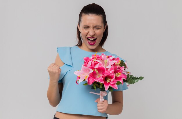 Excited pretty young woman holding bouquet of flowers and keeping fist